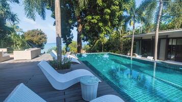 Una piscina con agua azul cristalina, rodeada de una terraza de madera y sillones de descanso.