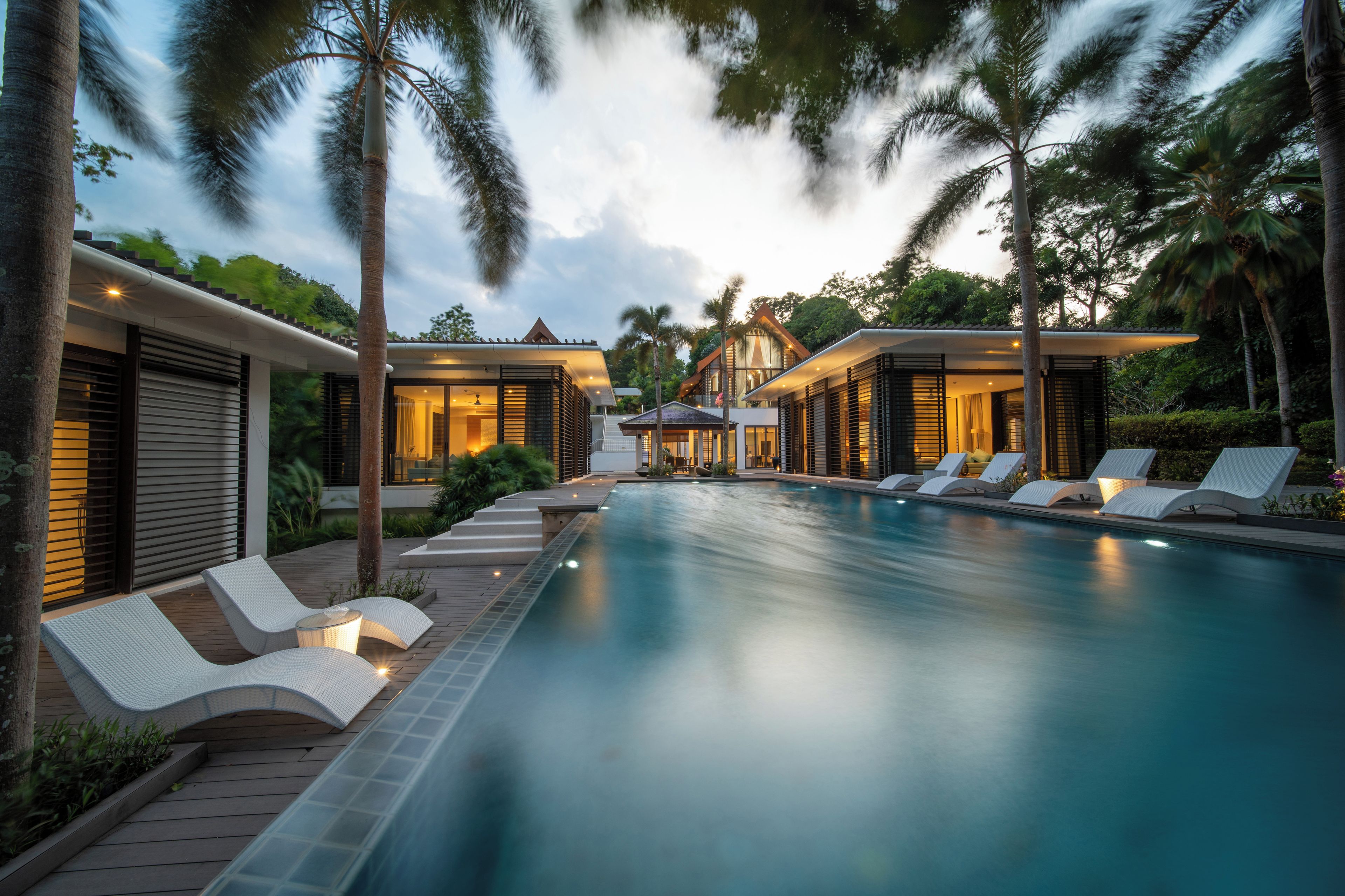 Un resort moderno con piscina, sillones de descanso y exuberante jardinería tropical.