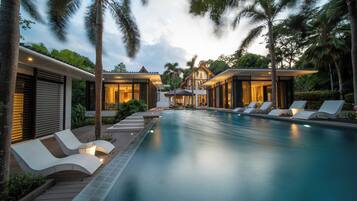 Un resort moderno con piscina, sillones de descanso y exuberante jardinería tropical.