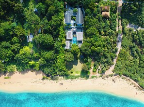 An aerial view of a beachfront property with a large house surrounded by dense greenery and a sandy beach. - Marina luxury 6-bedroom seaview villa (Thalang)