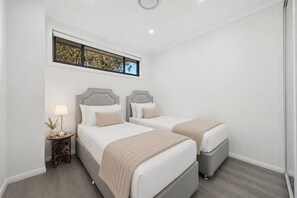 Una habitació d'hotel amb dos llits, una meseta de nit amb una làmpada i una finestra amb vista a arbres.