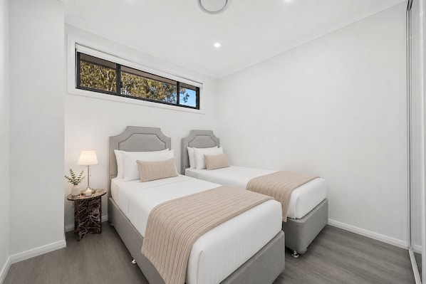A hotel room with two beds, a nightstand with a lamp, and a window with a view of trees.