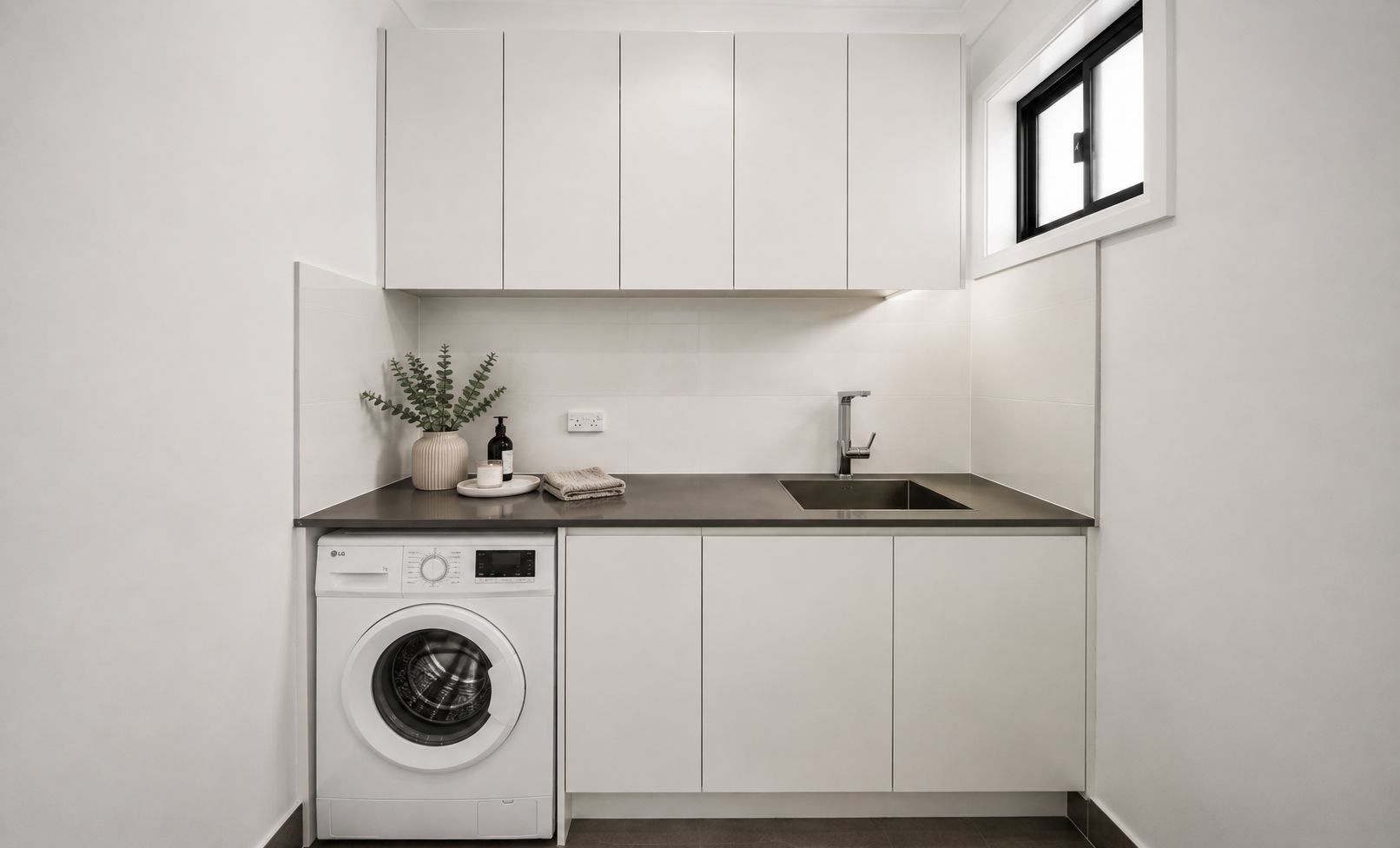 A compact laundry room with a washing machine, a sink, and cabinets.