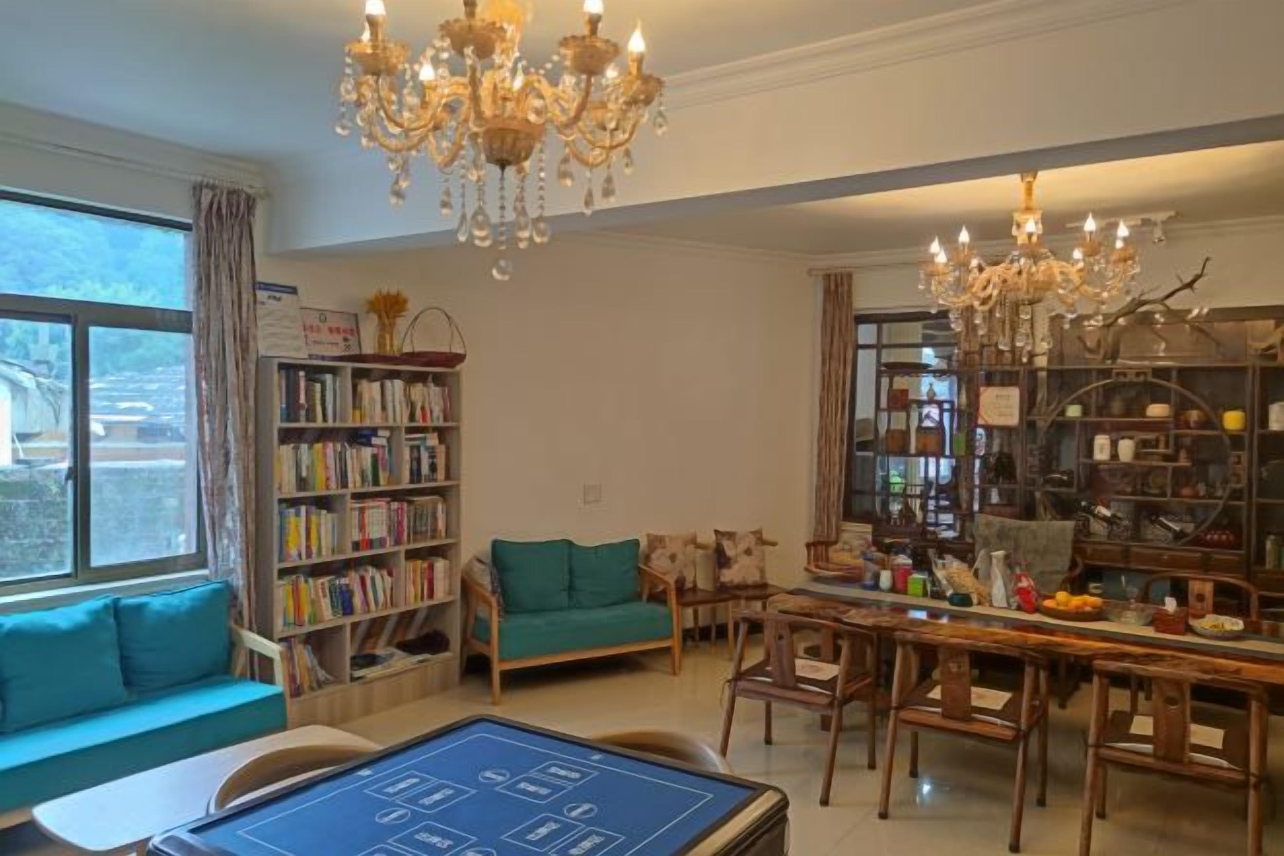 A spacious living room with a large window, a chandelier, a bookshelf, a sofa, and a dining area.