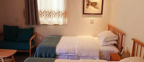 A room with two beds, a sofa, a table, and a window with curtains.