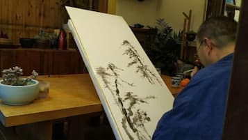 A person in a blue robe standing next to a table with a large white painting and a bowl of flowers.