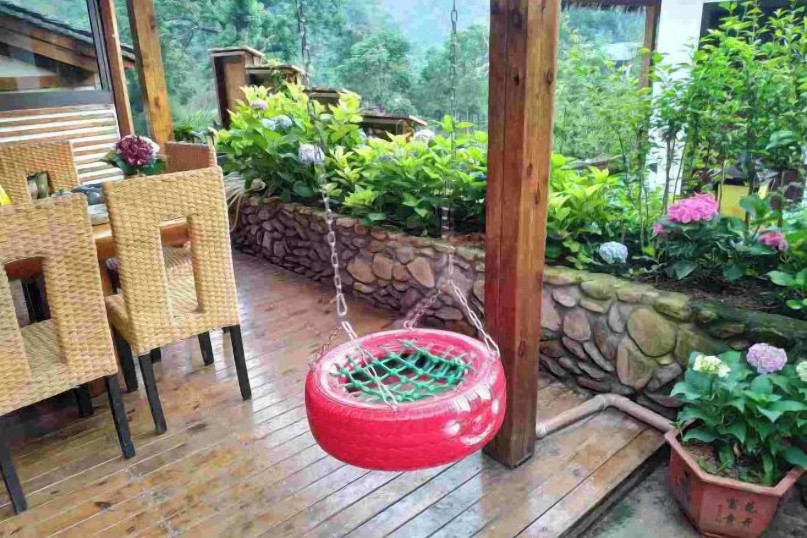 Una terraza de madera con mobiliario de mimbre, un columpio de neumático colgante y un muro de piedra con plantas en macetas.