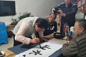 Un grupo de personas practicando caligrafía, con una hoja de papel grande sobre la mesa.