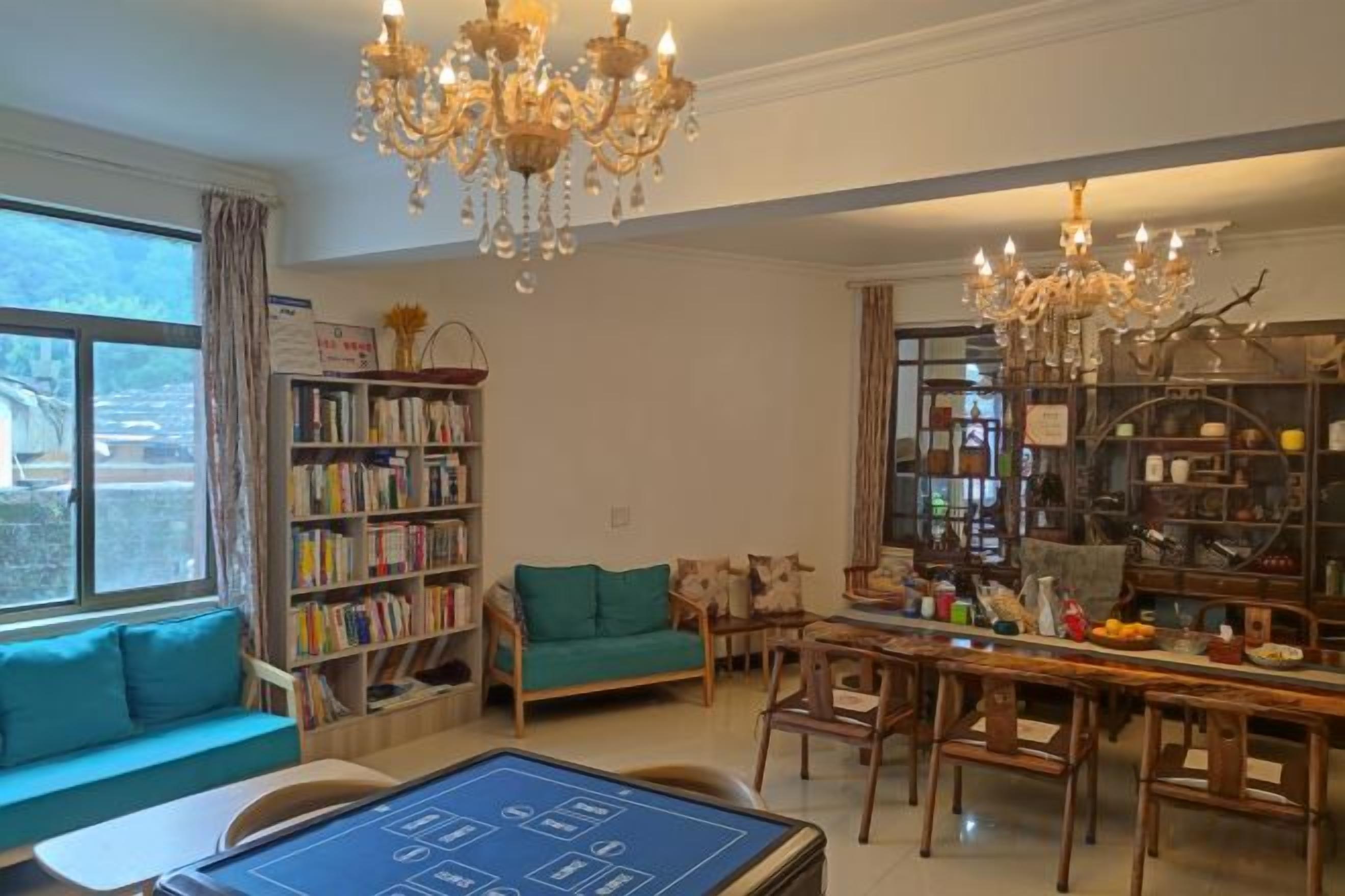 A spacious living room with a large window, a chandelier, a bookshelf, a sofa, and a dining area.