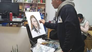 A person painting on a canvas in a room with shelves containing various items.