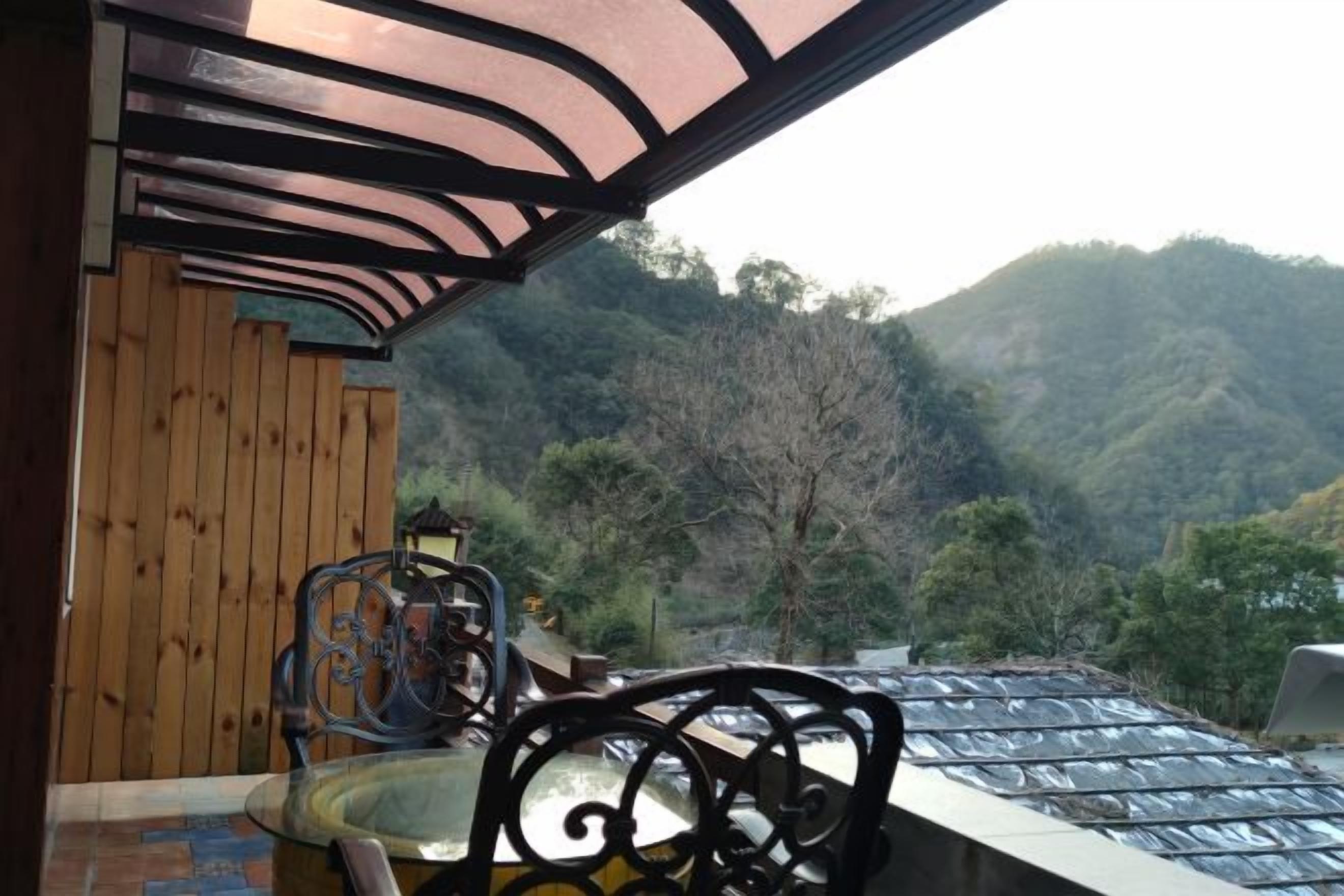 A balcony with a view of a mountainous landscape, a wooden wall, and a metal chair.