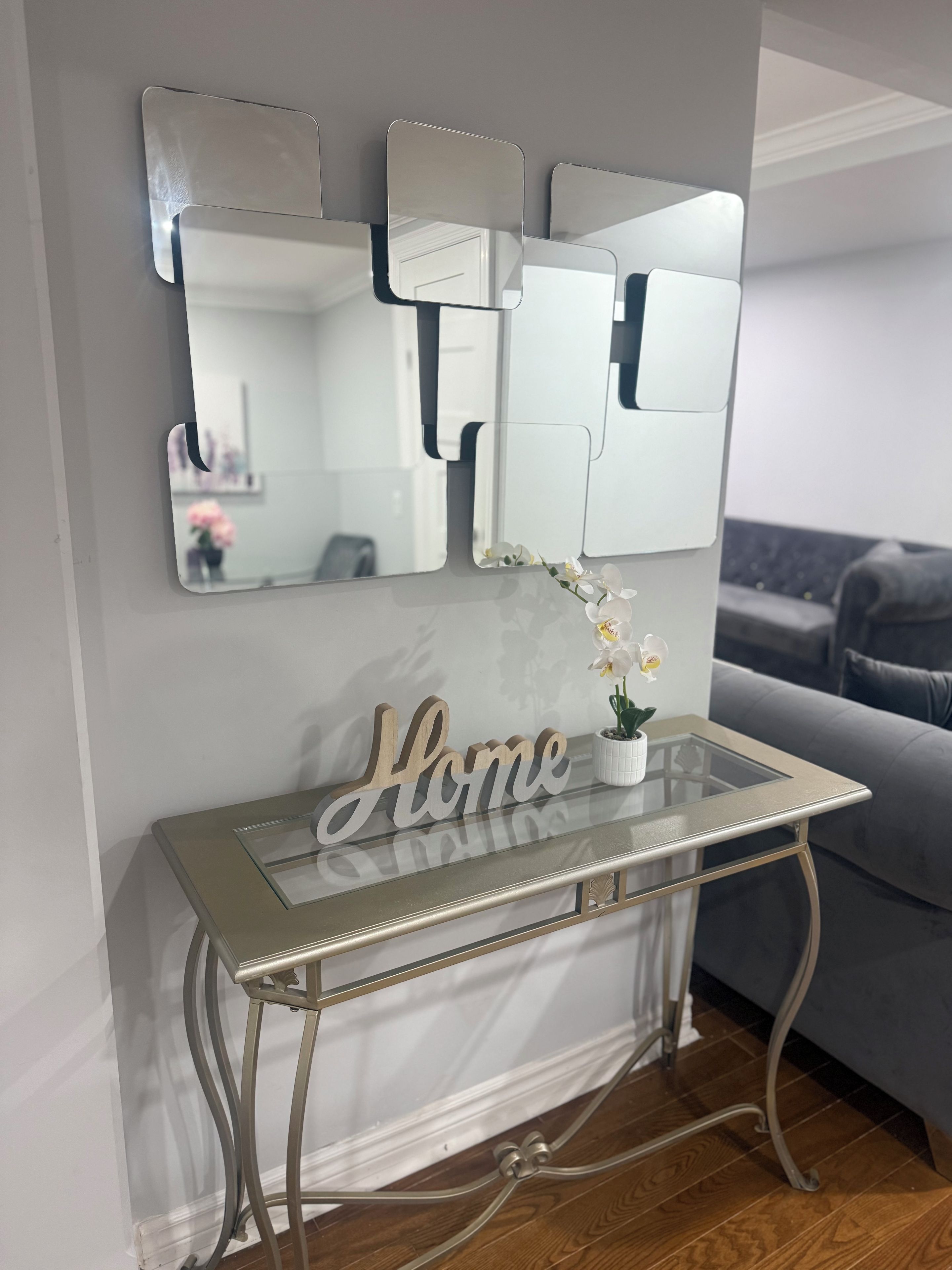 A room with a glass-top console table, a mirror, and a 'Home' sign.