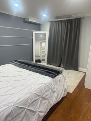 Ein Schlafzimmer mit Bett, Spiegel, Tür und einem Fenster mit Vorhängen.