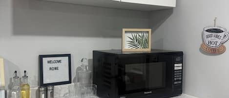 A kitchen with a white cabinet, a black microwave, and a welcome home sign.