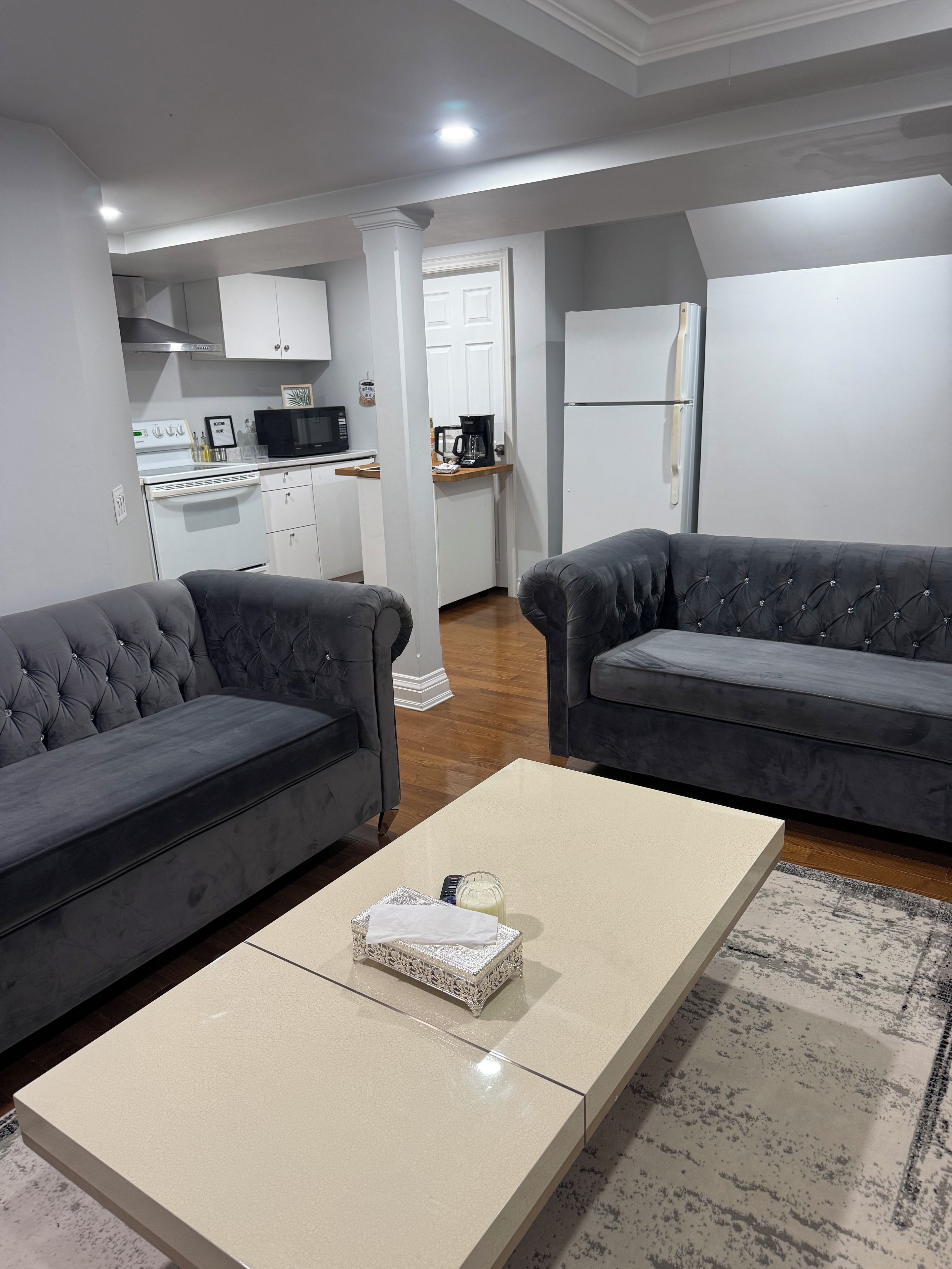 Un salon moderne avec deux canapés gris, une table basse beige et une cuisine en arrière-plan.
