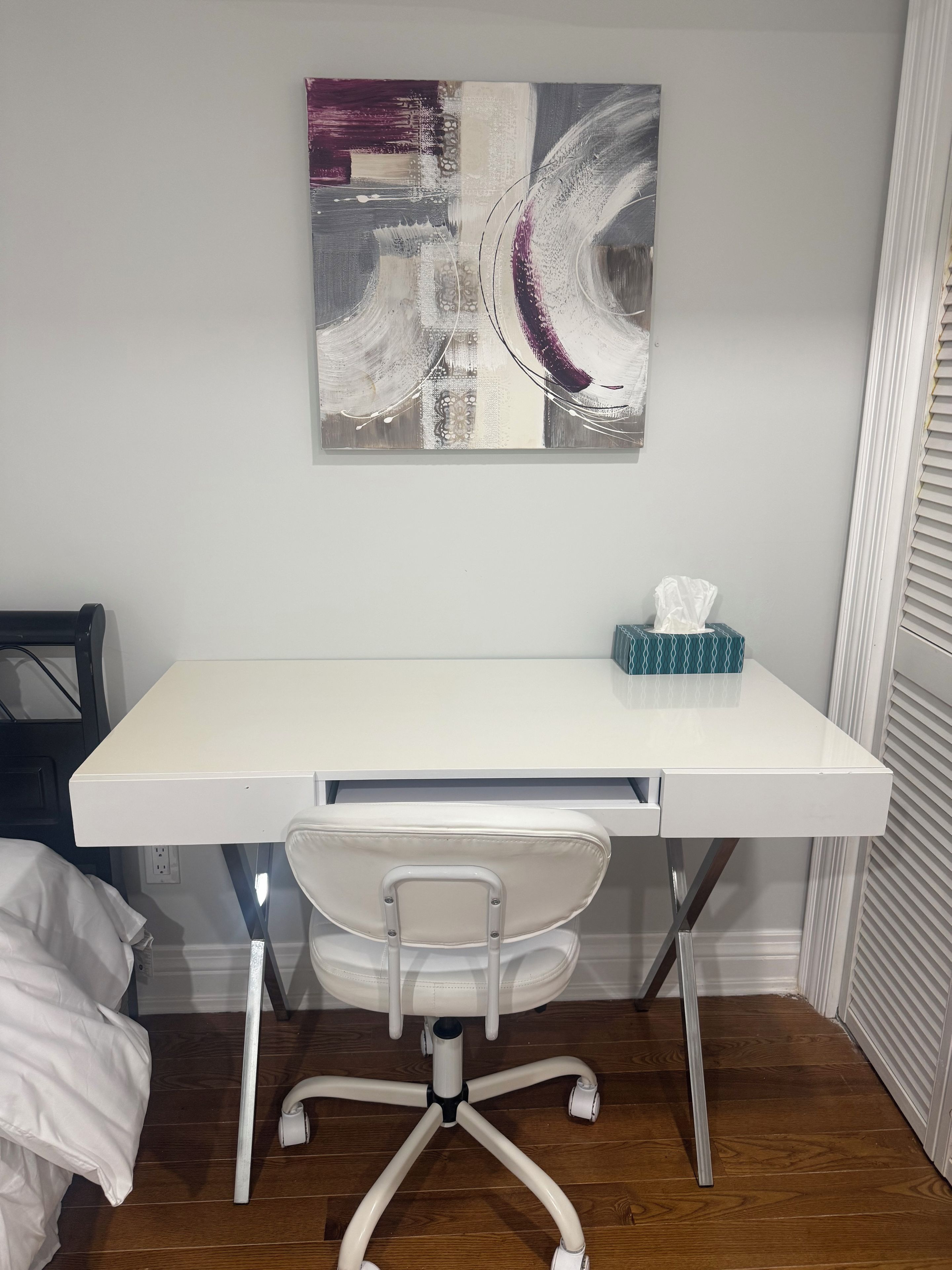 Un bureau blanc avec un ordinateur, une chaise et une œuvre d’art murale.