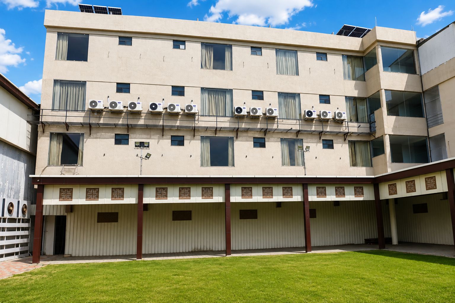 A multi-story building with air conditioning units, a covered parking area, and a well-maintained lawn.