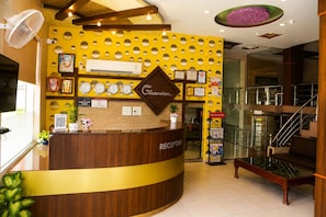 A reception area with a wooden reception desk, a yellow wall with circular cutouts, and a ceiling with recessed lighting. - Hotel Royal Celebration (Jaipur)