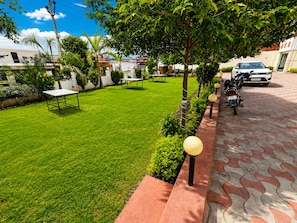 A well-maintained lawn with a picnic table, a paved walkway, and a parked motorcycle. - Hotel Royal Celebration (Jaipur)