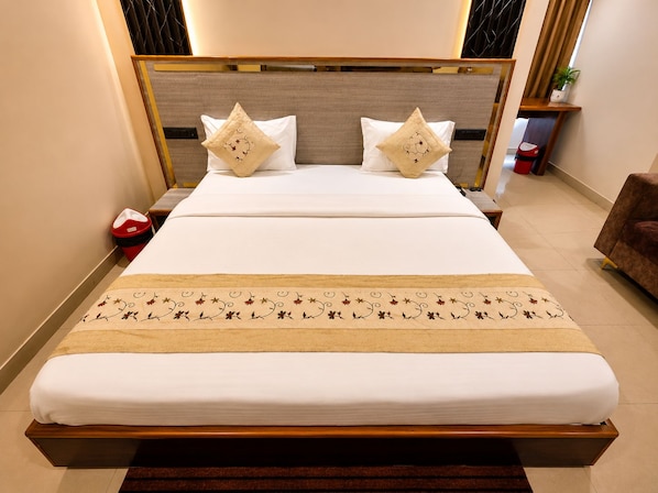 A neatly made bed with a wooden headboard, two decorative pillows, and a floral-patterned bed runner. - Hotel Royal Celebration (Jaipur)