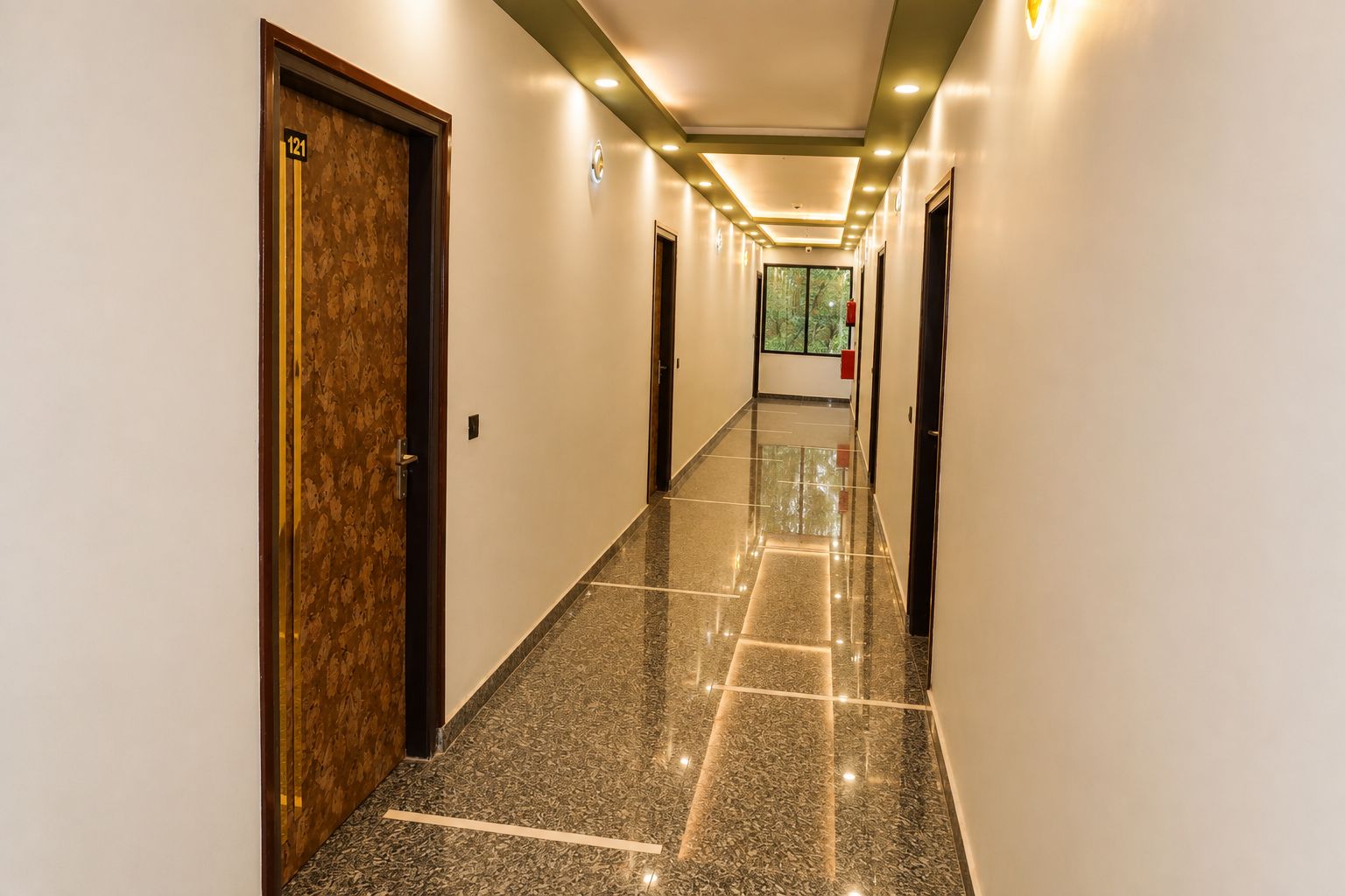 Corredor de hotel com piso de mármore, portas em ambos os lados e iluminação embutida.