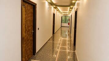 Corredor de hotel com piso de mármore, portas em ambos os lados e iluminação embutida.