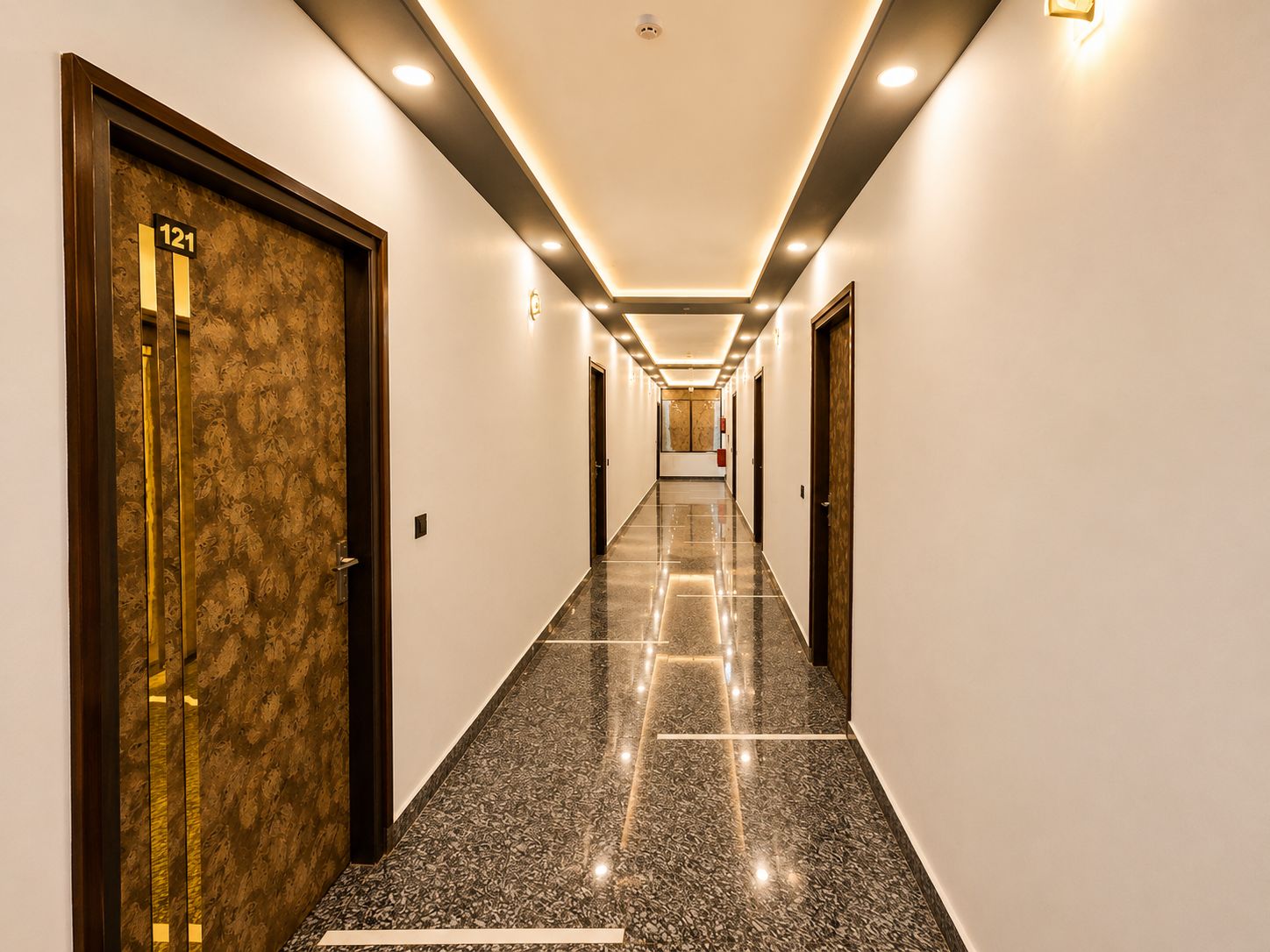 A hotel hallway with a marble floor, doors on both sides, and recessed lighting.