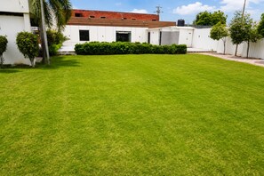 A well-maintained grassy yard with a white building, a red roof, and a water tank. - Hotel Royal Celebration (Jaipur)