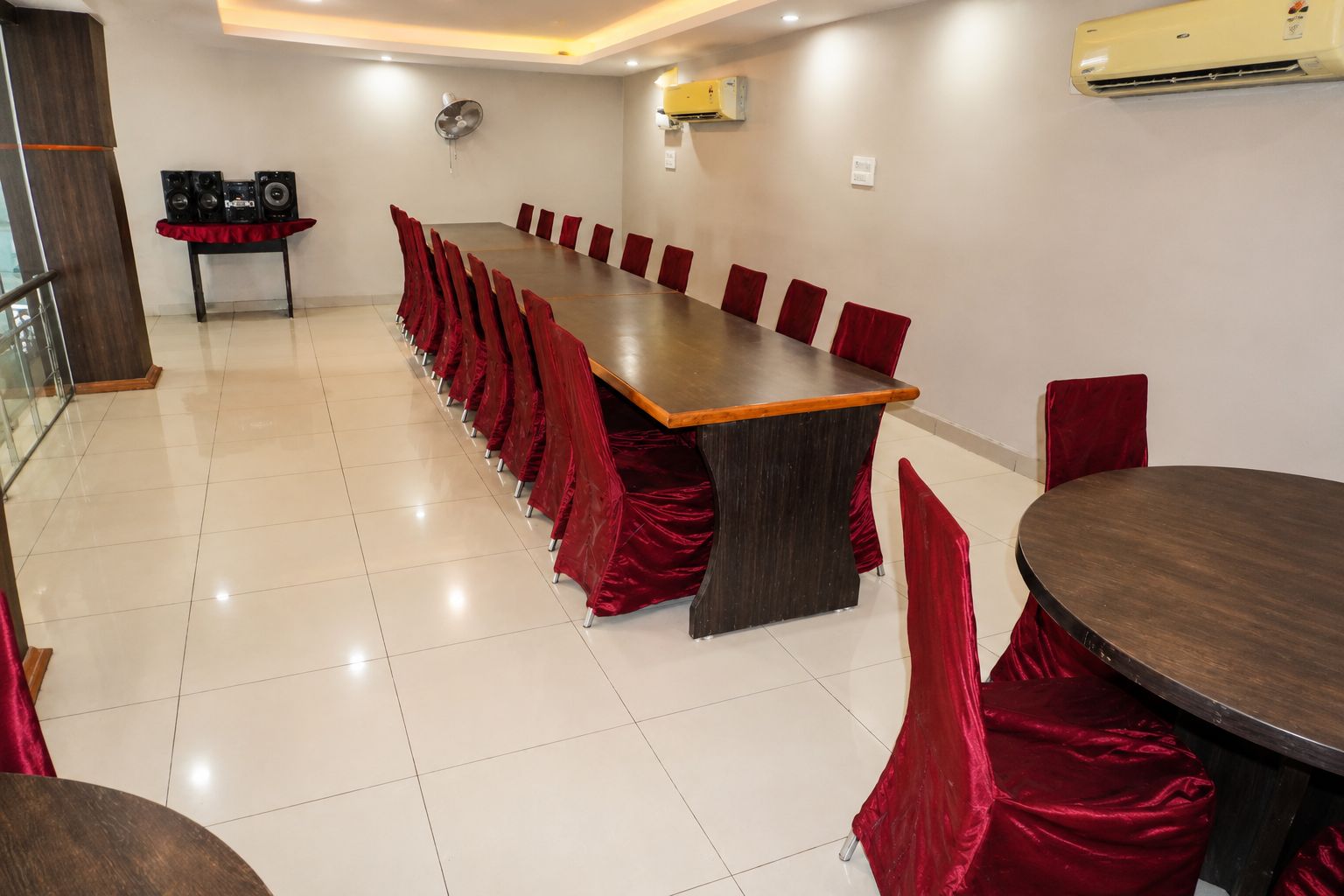 A conference room with a long table and red chairs, an air conditioning unit, and a speaker system.