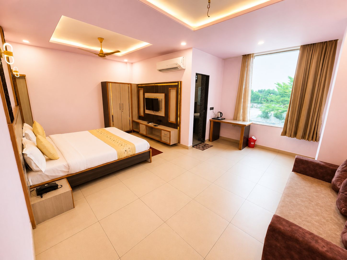 Quarto de hotel com cama, escrivaninha, televisão e janela com cortinas.