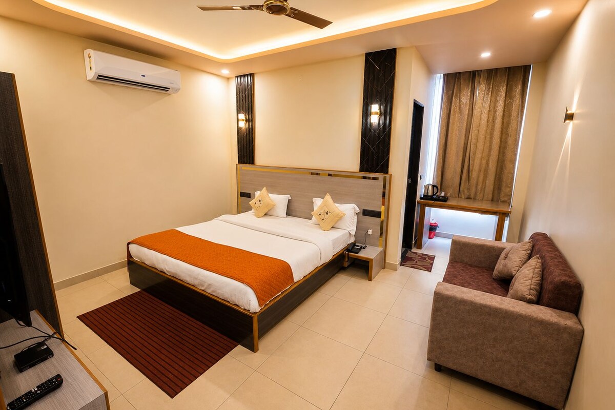 Une chambre d’hôtel comprenant un lit, un canapé, un ventilateur de plafond, un appareil de climatisation et une fenêtre avec des rideaux.