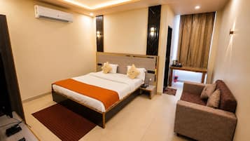 Habitación de hotel con cama, sofá, ventilador de techo, aire acondicionado y ventana con cortinas.