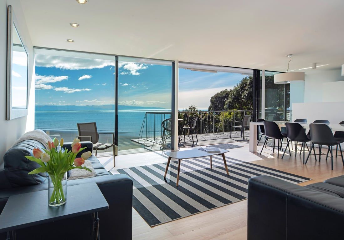 Ein modernes Wohnzimmer mit einem großen Glasfenster, das auf einen Balkon mit Blick auf ein Gewässer führt.