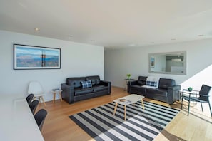 A modern living room with two black leather sofas, a white coffee table, and a black and white striped rug. - Beachfront Retreat - Architectural & Ocean Views (Nelson)