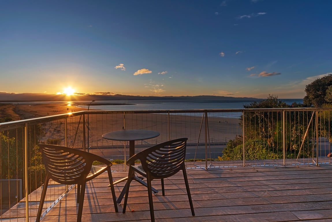 Een terras met een tafel en twee stoelen, met uitzicht op een waterpartij en veraf gelegen land.