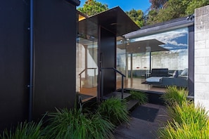 A modern house with a glass door leading to a living area with a sofa and a coffee table. - Beachfront Retreat - Architectural & Ocean Views (Nelson)