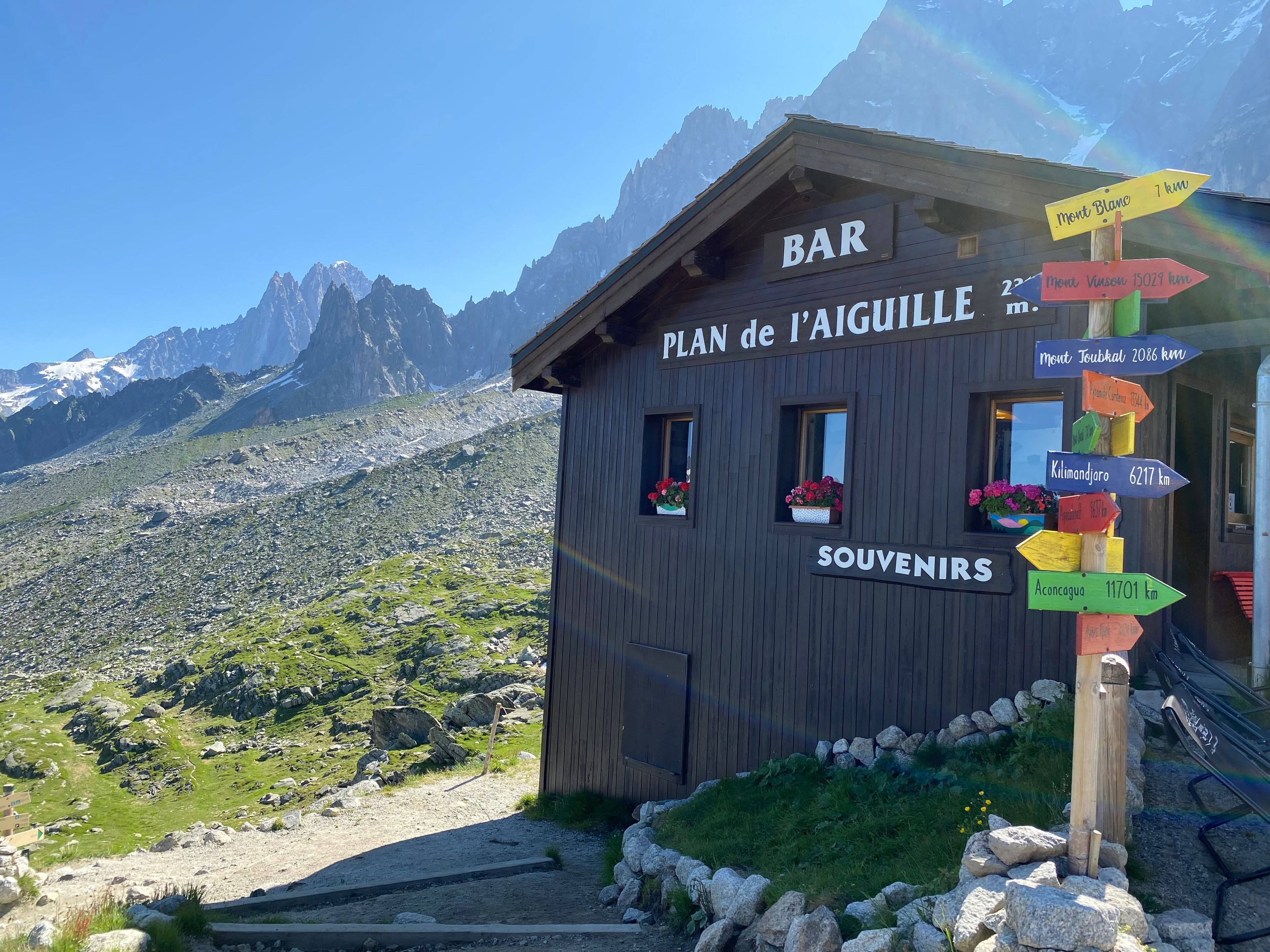 Un refuge de montagne en bois, avec une pancarte indiquant les distances vers différents sommets et un bar.