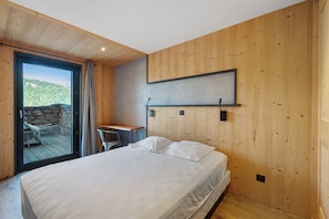 Ein Schlafzimmer mit Bett, Schreibtisch und Blick auf eine Berglandschaft durch eine Glasdoor.