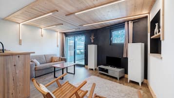 A modern living room with a sofa, wooden chairs, a coffee table, a TV, and a cabinet.