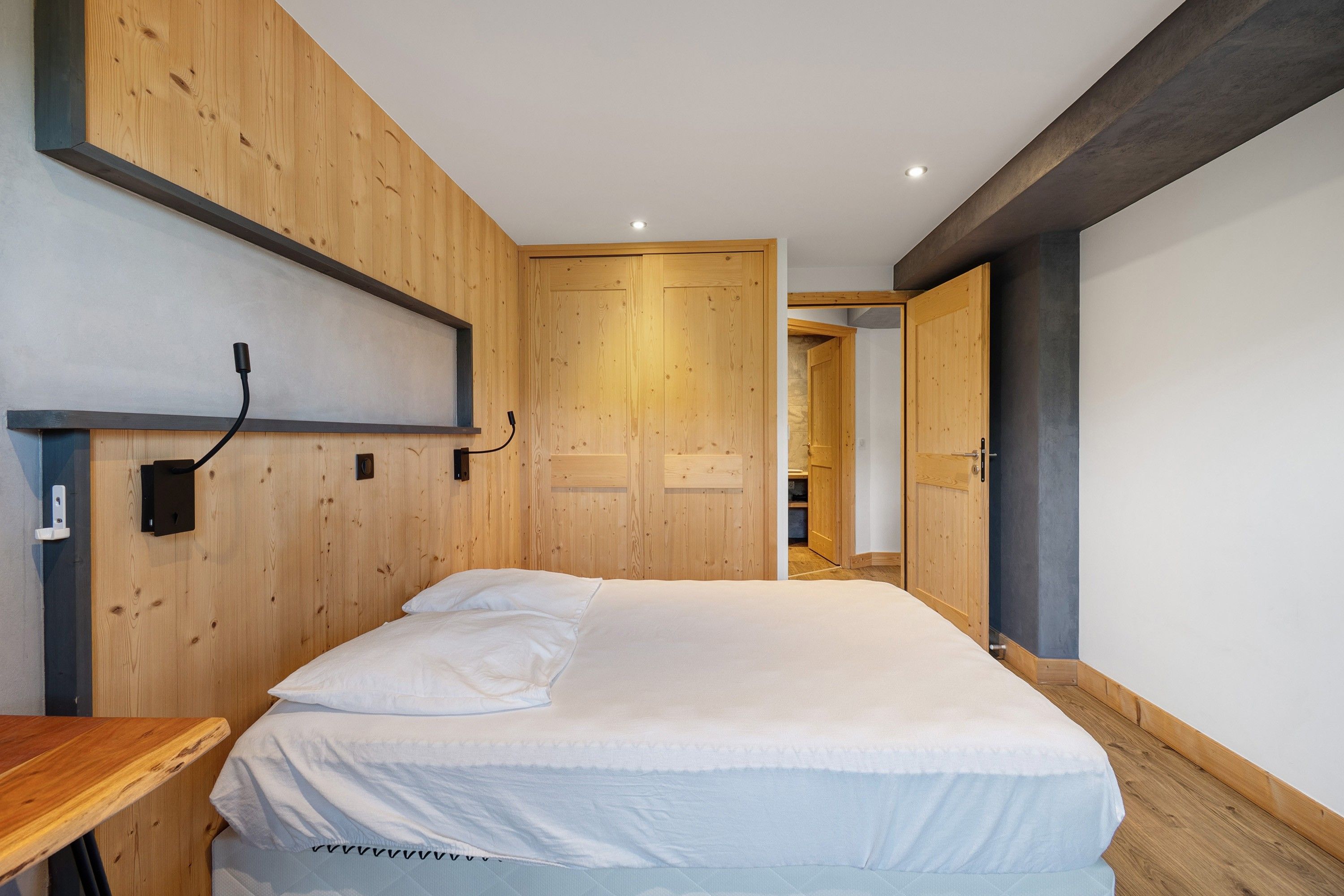 Ein Schlafzimmer mit einem hölzernen Kopfteil, einem Bett mit weißer Bettwäsche, einem Nachttisch und einer Holztür.