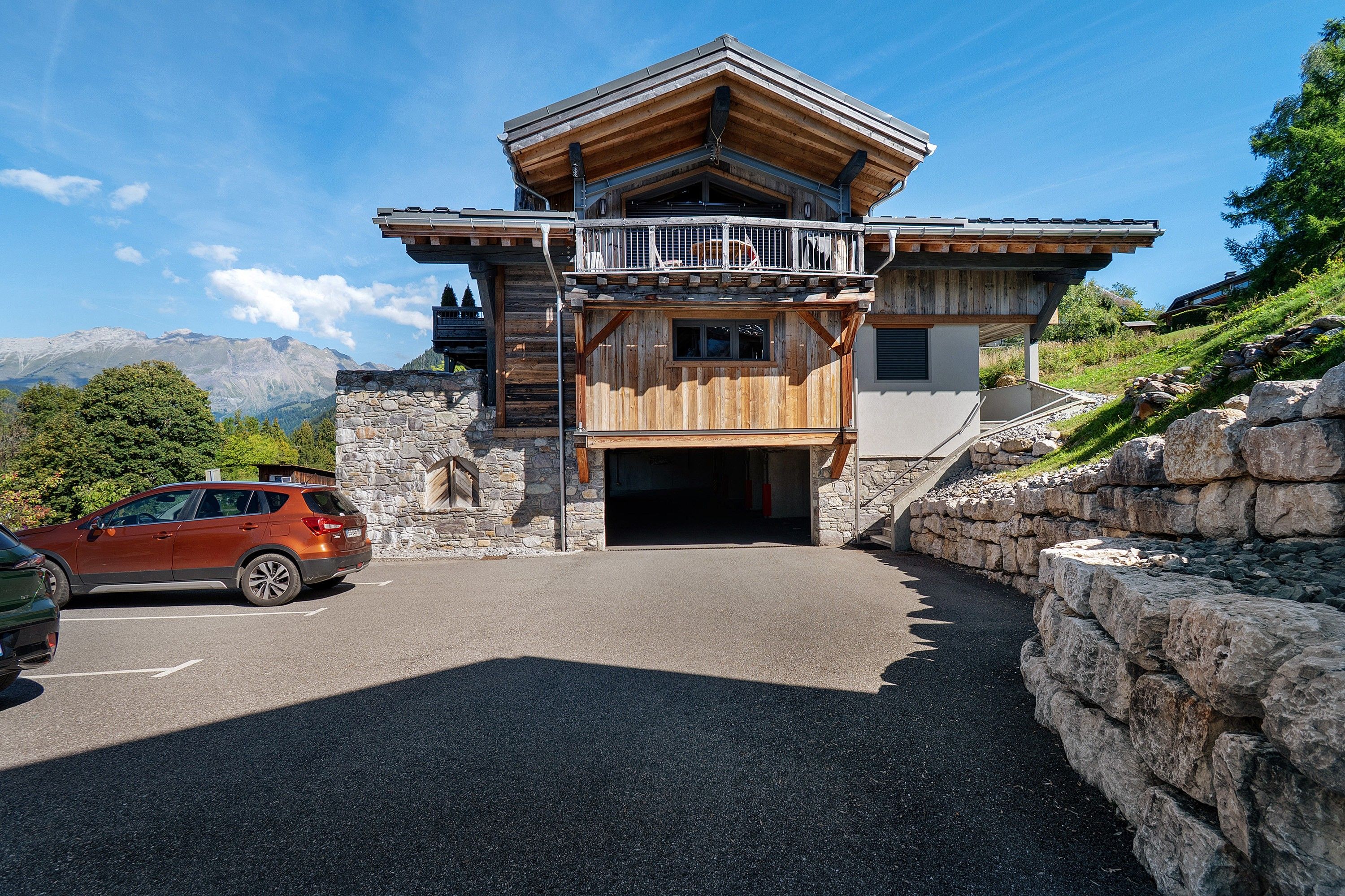 Un chalet de montagne avec une façade en pierre, un balcon en bois et une entrée de garage.