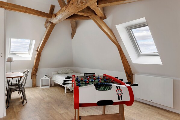 A loft bedroom with a wooden ceiling, a bed, a foosball table, and two skylights.