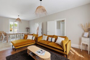 A modern living room with a large sectional sofa, a wooden coffee table, and a dining area with a white table and chairs.