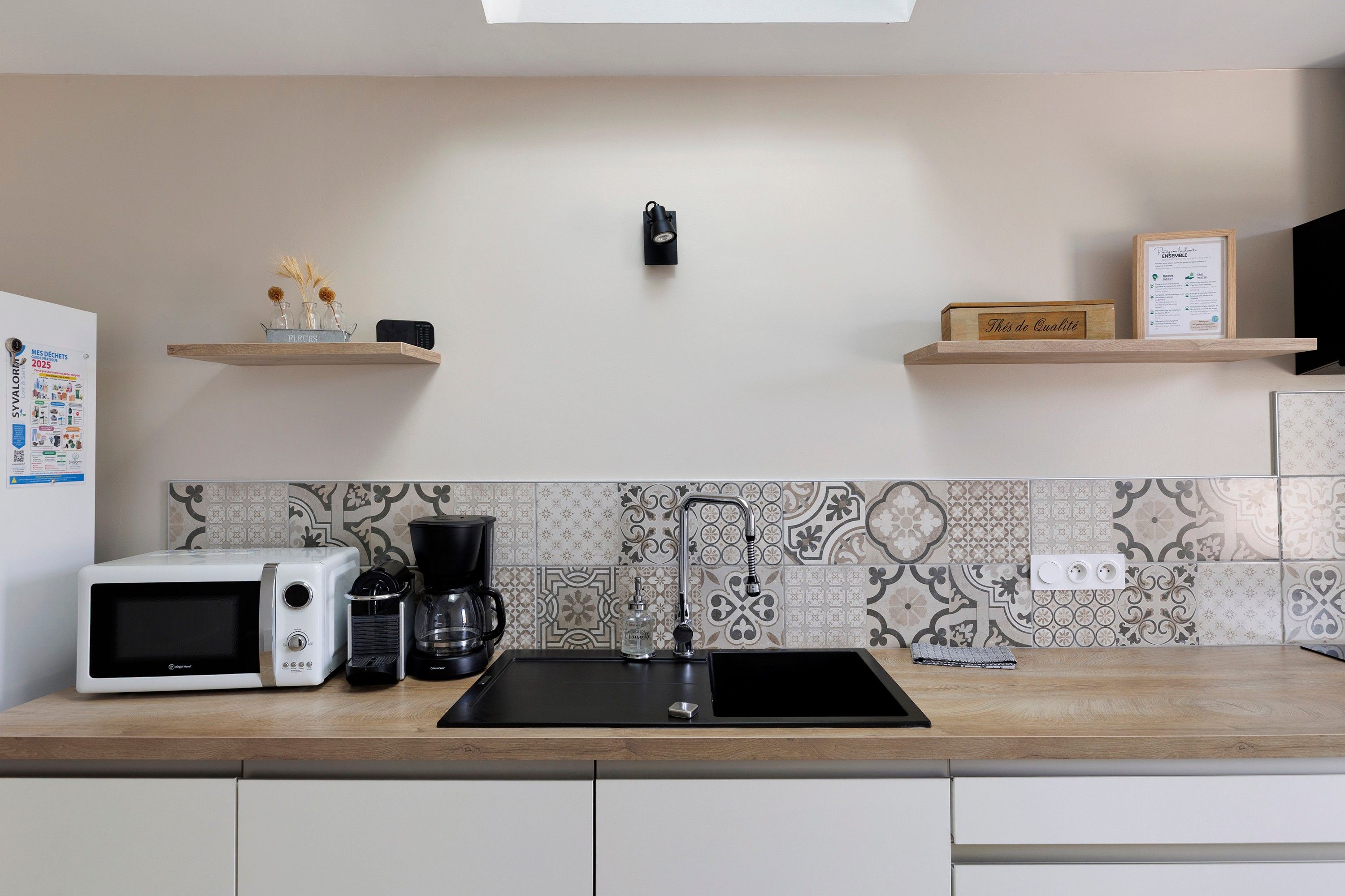 Una cucina moderna con un lavello nero, elettrodomestici bianchi e oggetti decorativi sugli scaffali.