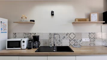 Una cucina moderna con un lavello nero, elettrodomestici bianchi e oggetti decorativi sugli scaffali.