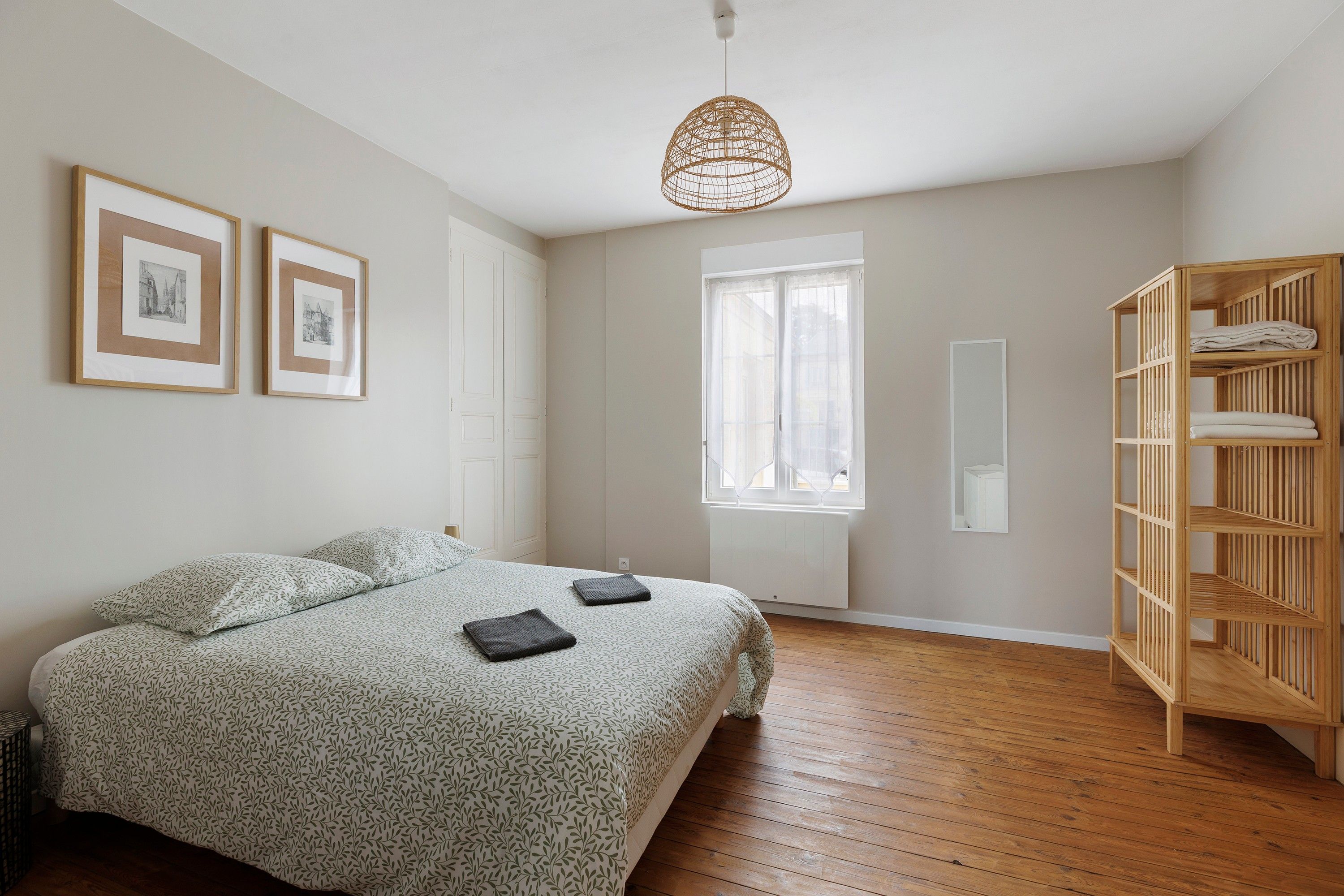 A bedroom with a bed, a wooden wardrobe, a window, and two framed pictures on the wall.