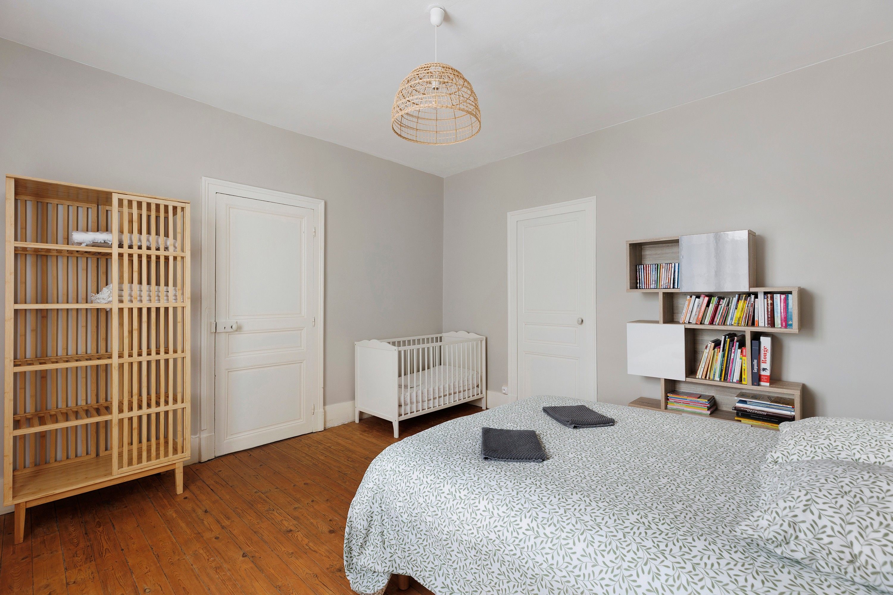 Une chambre à coucher avec un berceau, une armoire, une bibliothèque et un luminaire suspendu.
