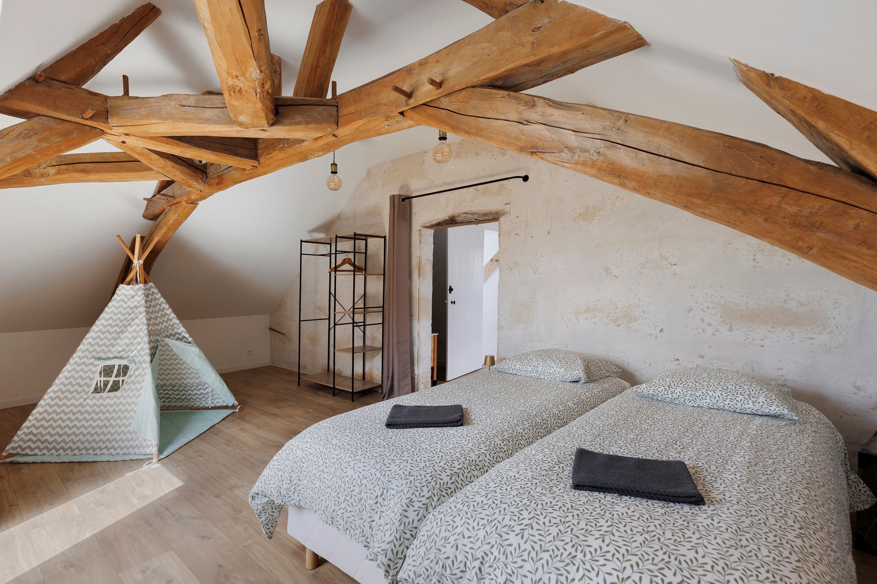Une chambre avec un plafond en pente, des poutres apparentes, un lit avec une literie à motifs, un luminaire suspendu et une petite armoire suspendue.