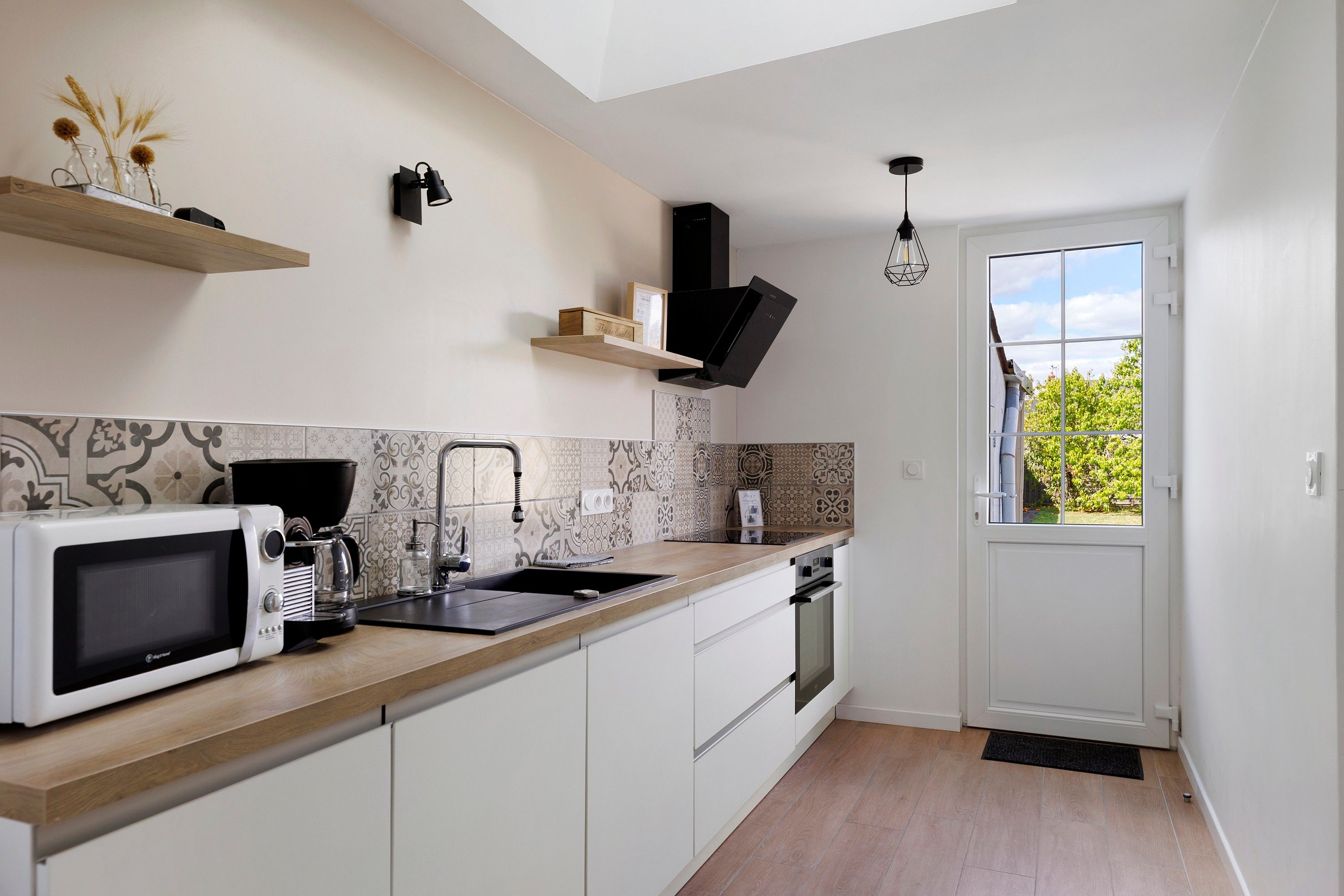 A modern kitchen with a microwave, coffee maker, and a sink. There is a window with a view of greenery outside.