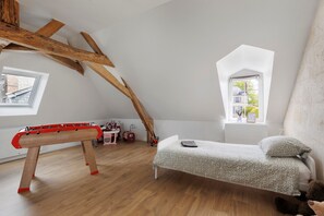 A room with a loft bed, a red foosball table, a window with a view, and wooden beams.